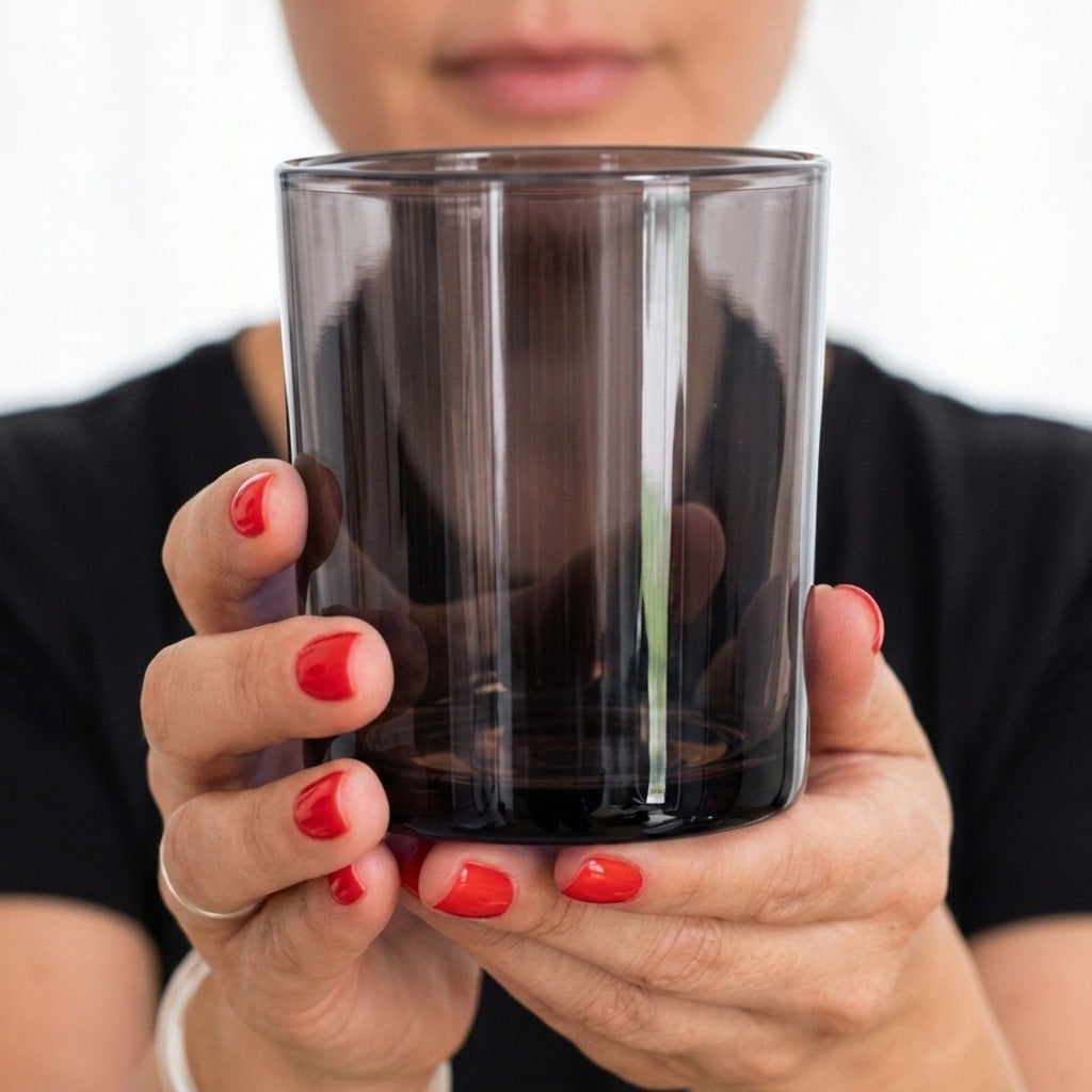 Hands holding a 10 oz translucent smoky black glass candle jar