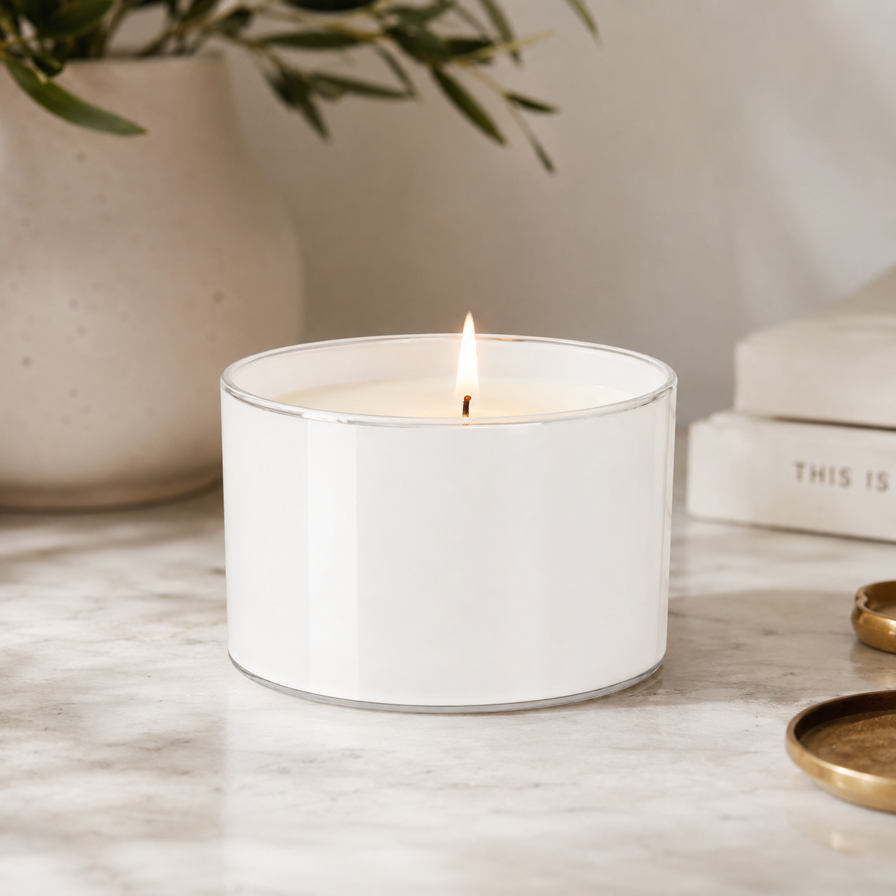BoroLux glass candle jar with white interior coating, lit soy candle, styled on marble with books and a vase